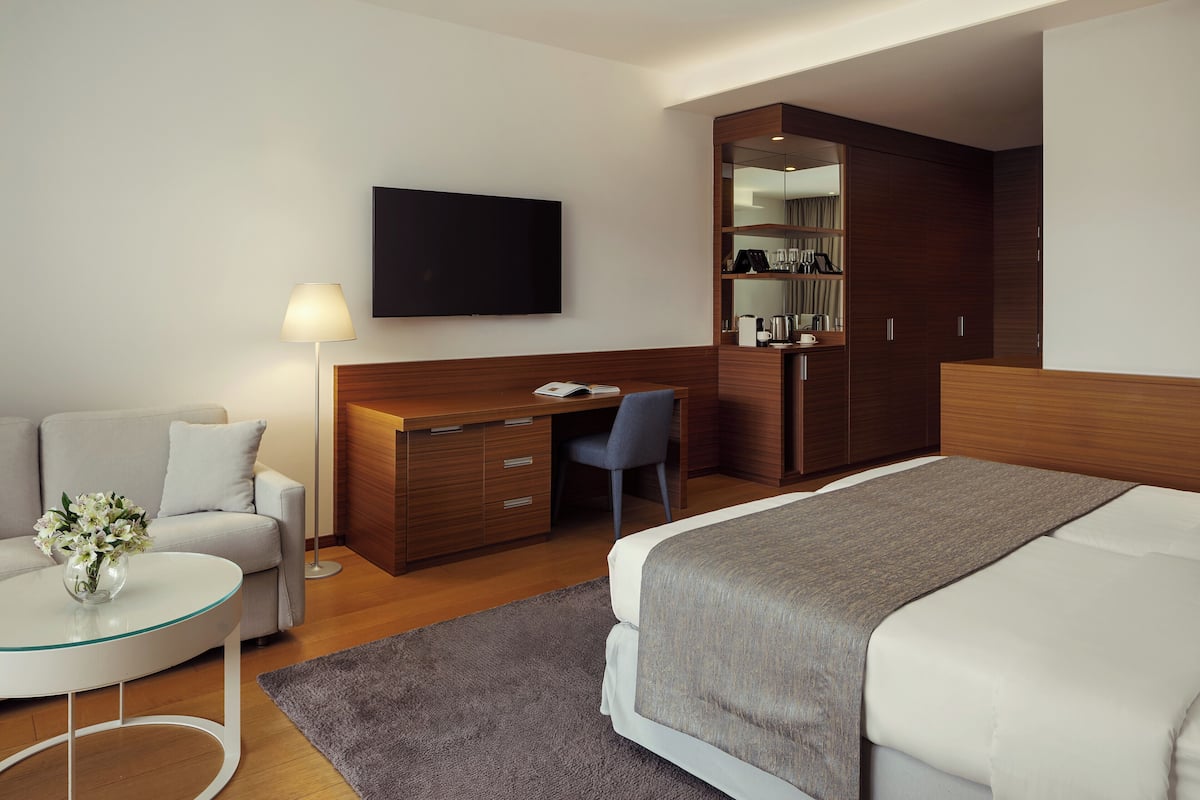 Ein Hotelzimmer mit Bett, Schreibtisch, Stuhl, Fernseher, Sofa und Couchtisch.