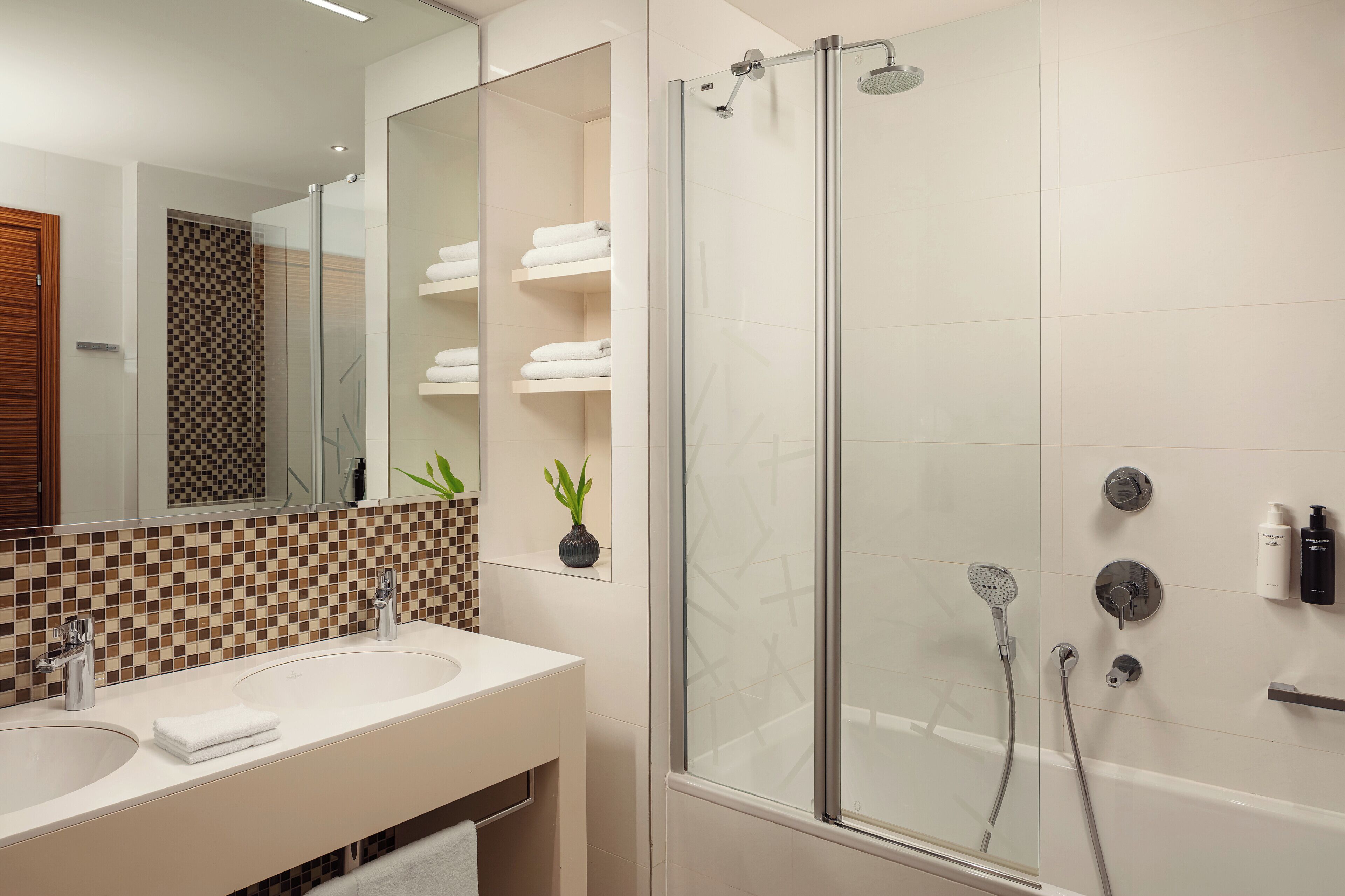 A modern bathroom with a glass-enclosed shower, a large mirror, and a checkered tile backsplash.