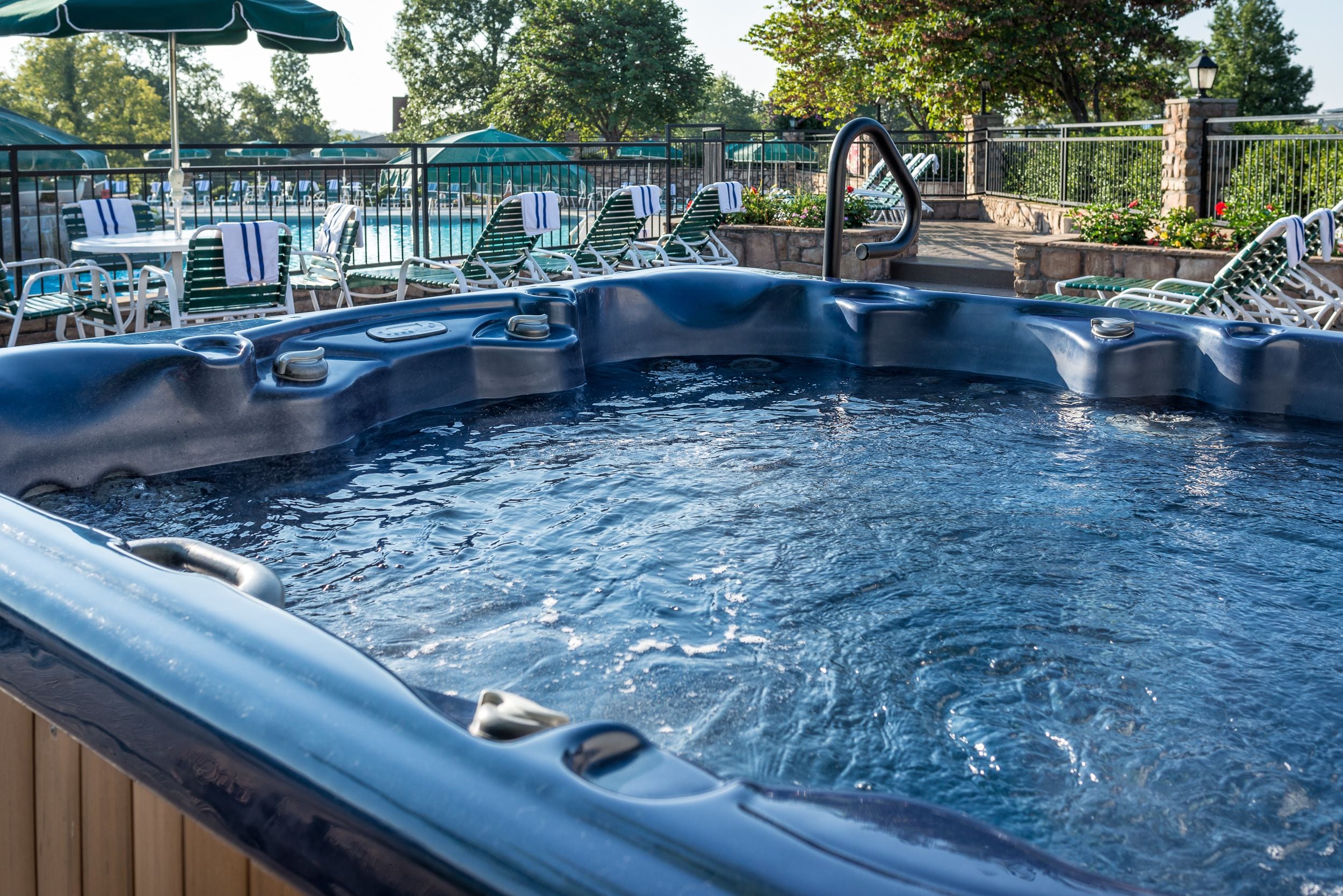 Un jacuzzi con cubierta de madera, rodeado de sillones de descanso y sombrillas.