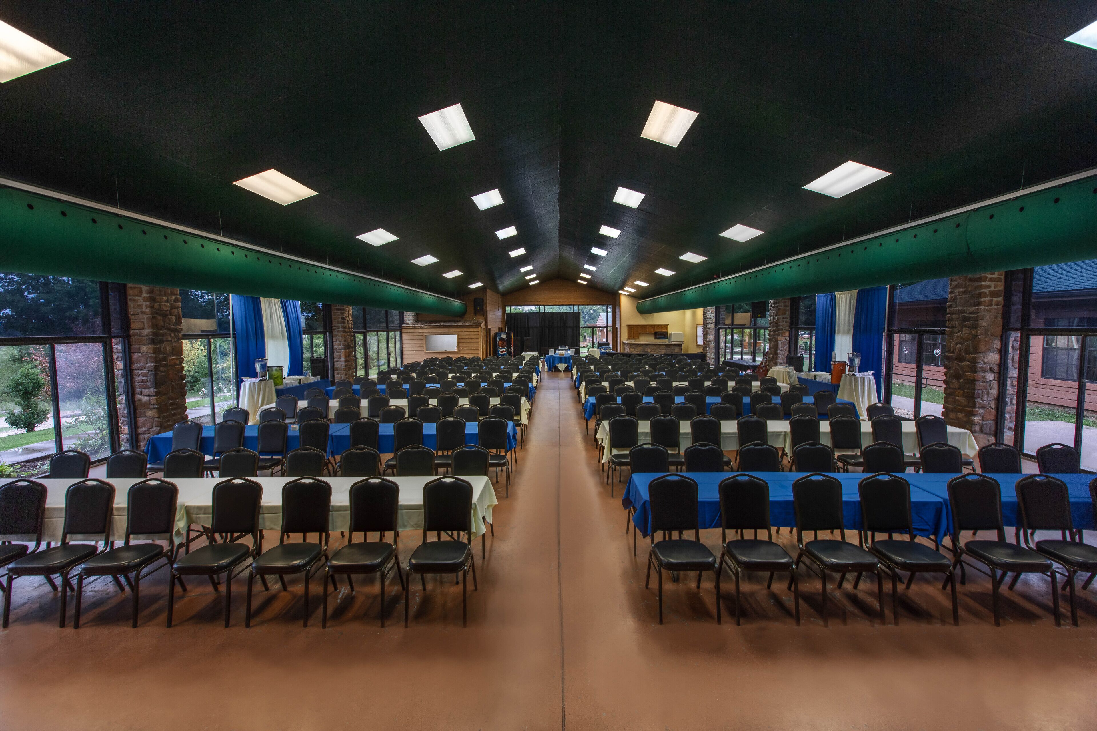 A large conference room with rows of tables and chairs, large windows, and a high ceiling with lighting fixtures.