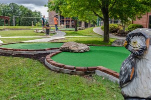 A miniature golf course with a putting green, a wooden sculpture, and a brick border.