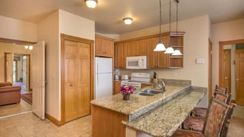 A kitchen with wooden cabinets, a granite countertop, a built-in microwave, a stove, and a sink. There are hanging pendant lights and a chair with a patterned cushion.