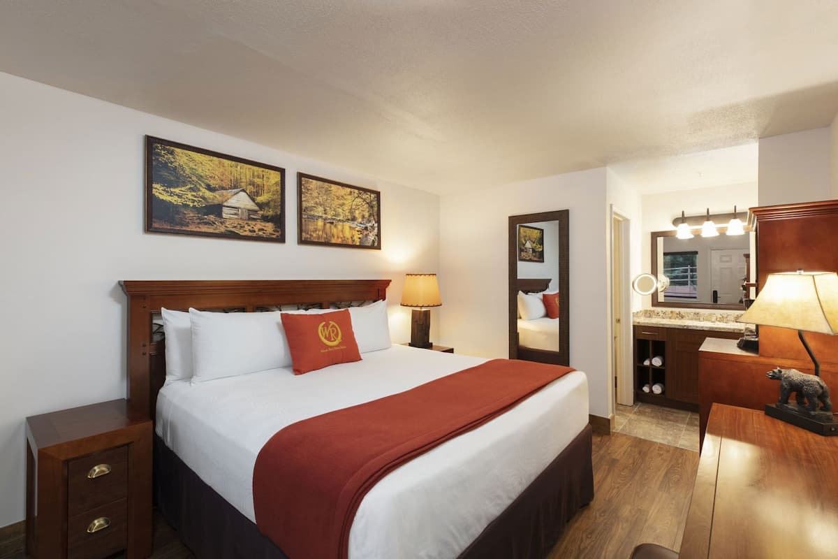 Een hotelkamer met een bed, een nachtkastje, een dressoir, een spiegel en twee ingelijste foto's aan de muur.