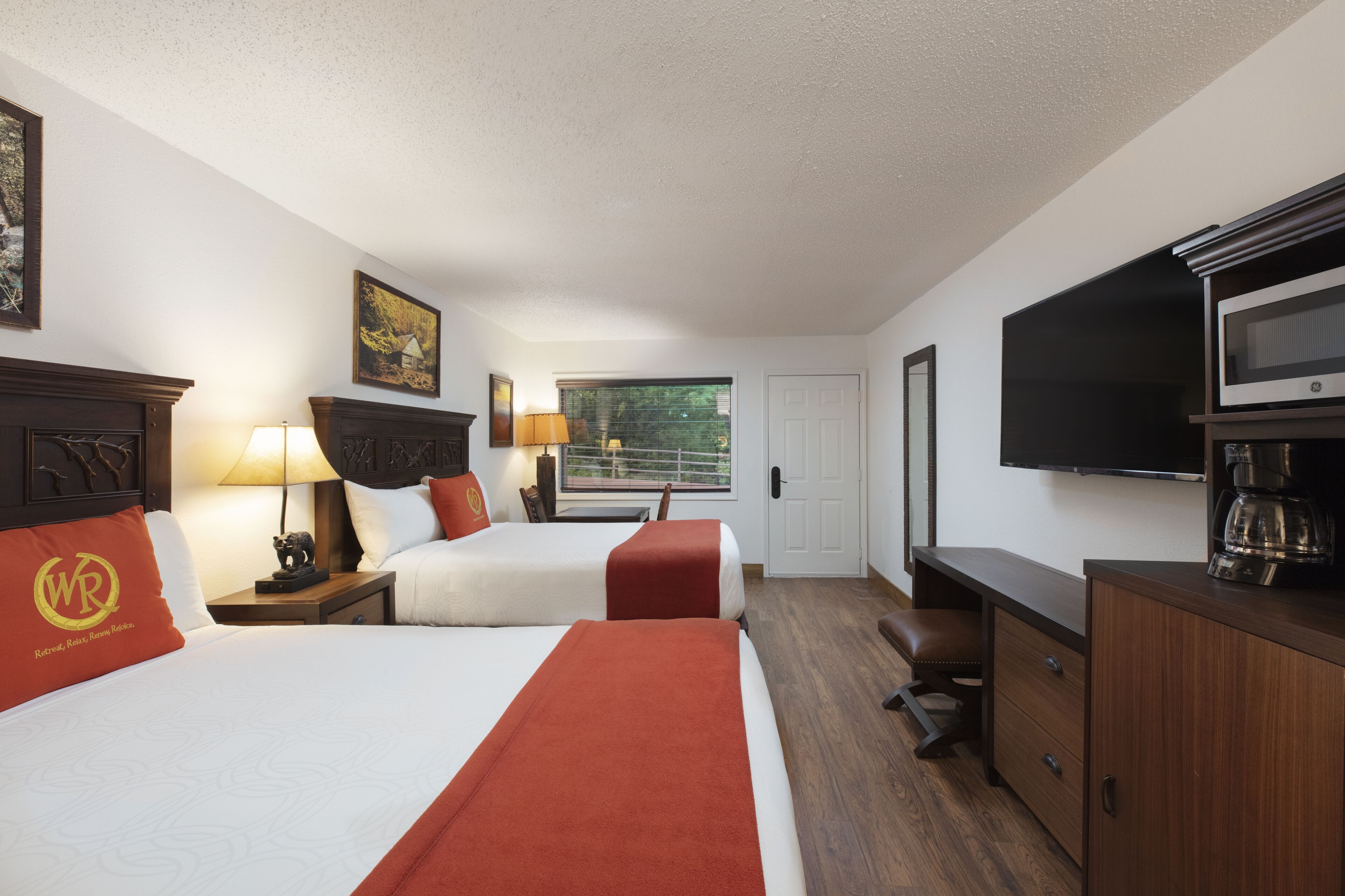 A hotel room with two beds, a TV, a coffee maker, and a desk.