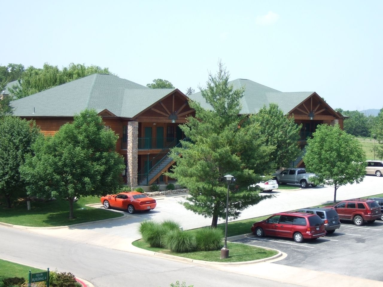 A building with a stone facade and a green roof, surrounded by a parking lot and trees.
