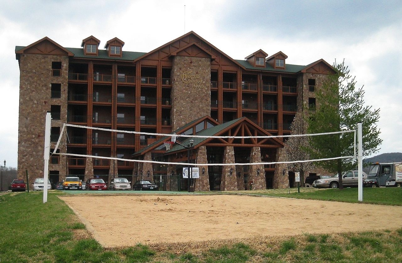 A large building with multiple floors, a stone facade, and a green roof. There is a volleyball net in front of the building.