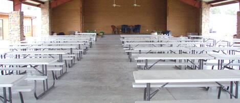 Een ruime binnenruimte met rijen witte picknicktafels en een hoog plafond met metalen balken.