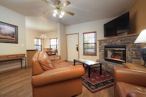 Una sala de estar con un sofá de cuero, una mesa de centro, una chimenea, un televisor y una araña.