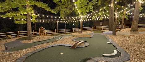 Un campo de mini golf de noche con iluminación artificial y una valla de madera.