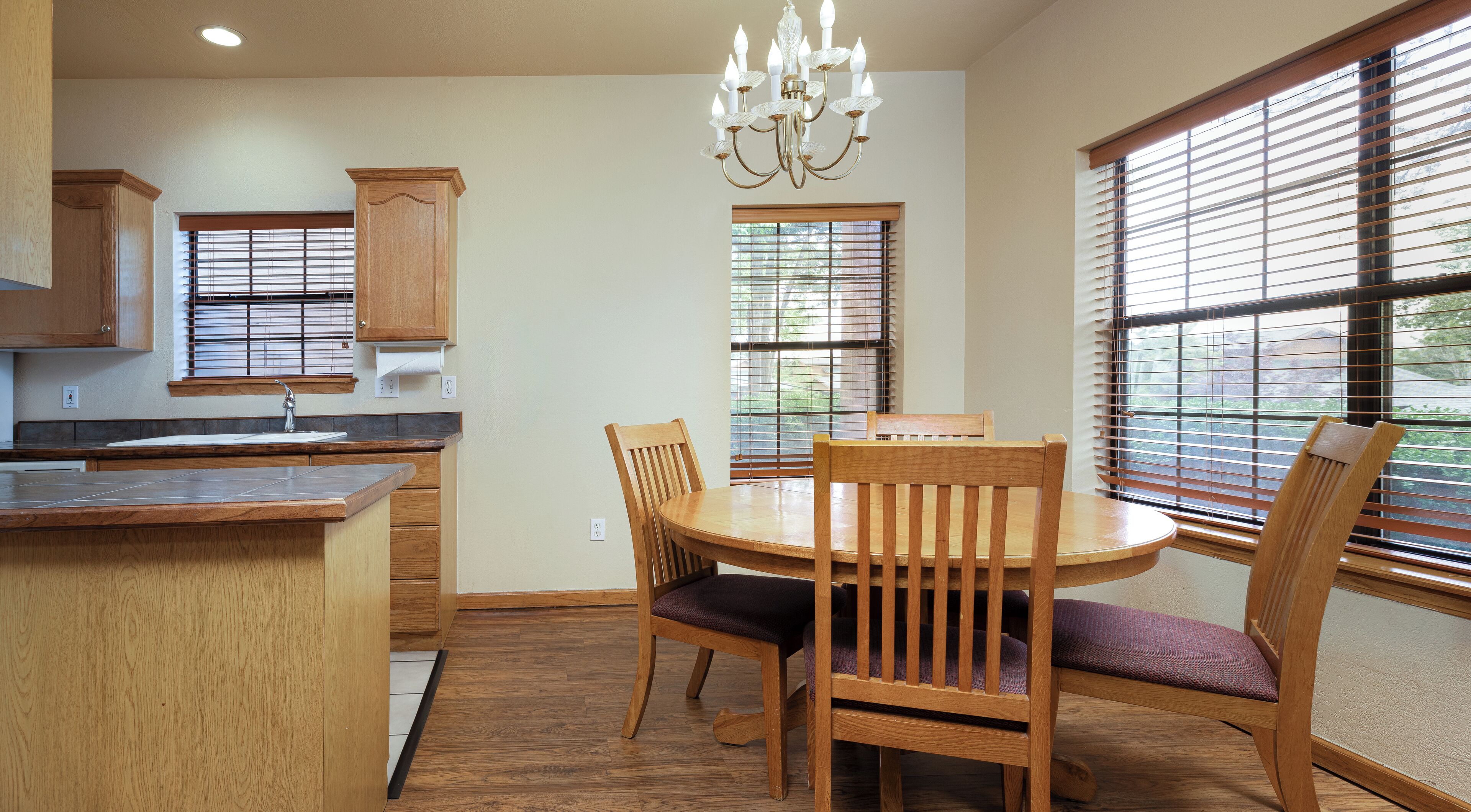 A kitchen with wooden cabinets, a dining table with chairs, and large windows with blinds.