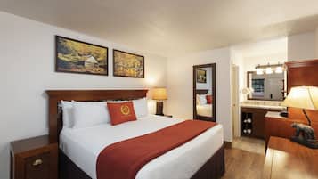 Een hotelkamer met een houten bed, een nachtkastje, een dressoir, een spiegel en twee ingelijste foto's aan de muur.