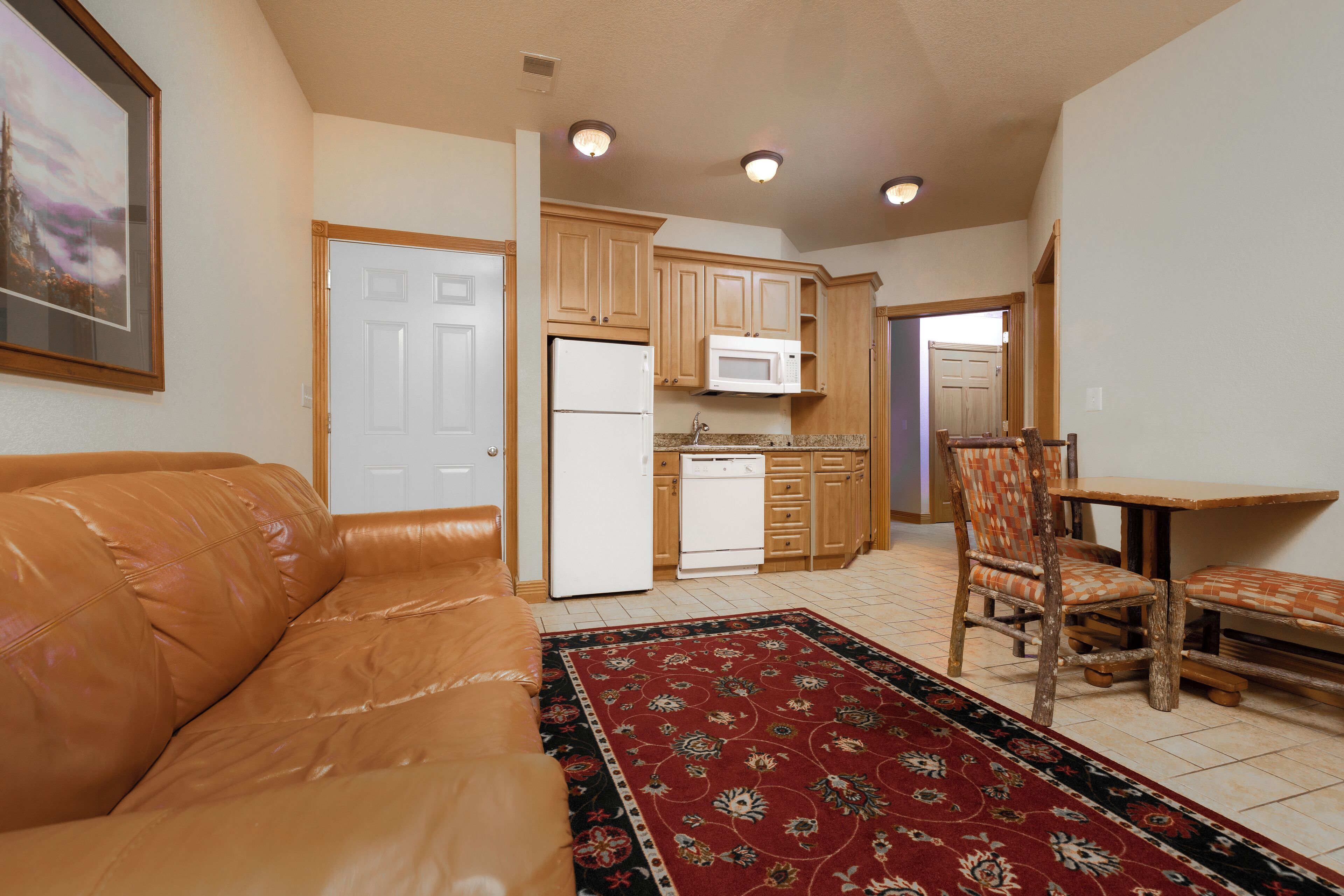 A compact living space with a kitchenette, a dining area with a wooden table and chairs, and a leather sofa.