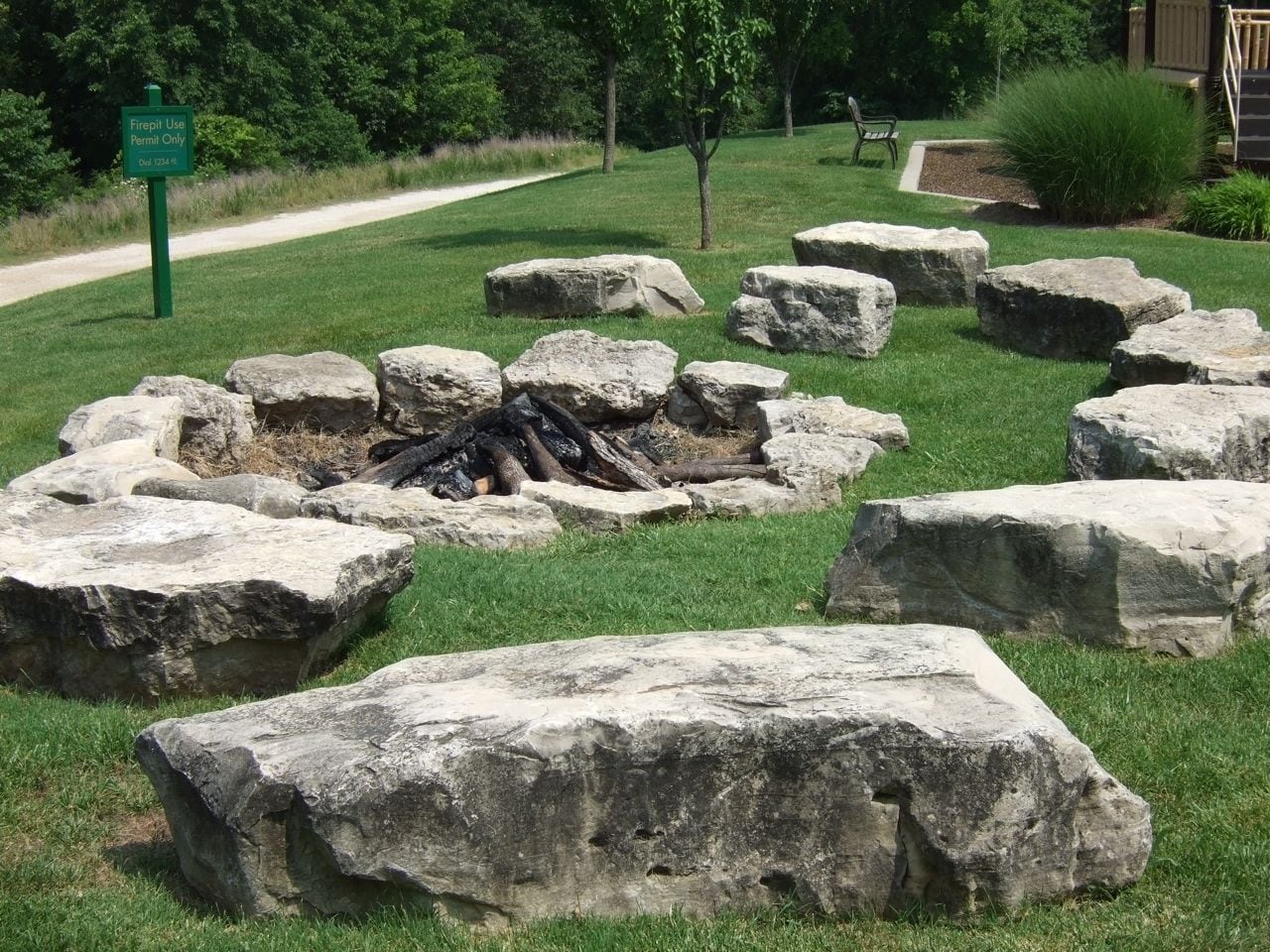 A fire pit surrounded by large rocks in a grassy area with a sign indicating fire use permit only.