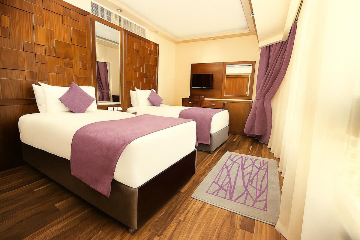 A hotel room with two beds, wooden headboard panels, a flat-screen TV, a mirror, and a bathroom with a shower curtain.