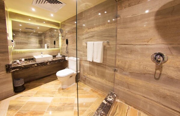 Un baño moderno con cabina de ducha de vidrio, paredes de mármol y un tocador con lavamanos y espejo.