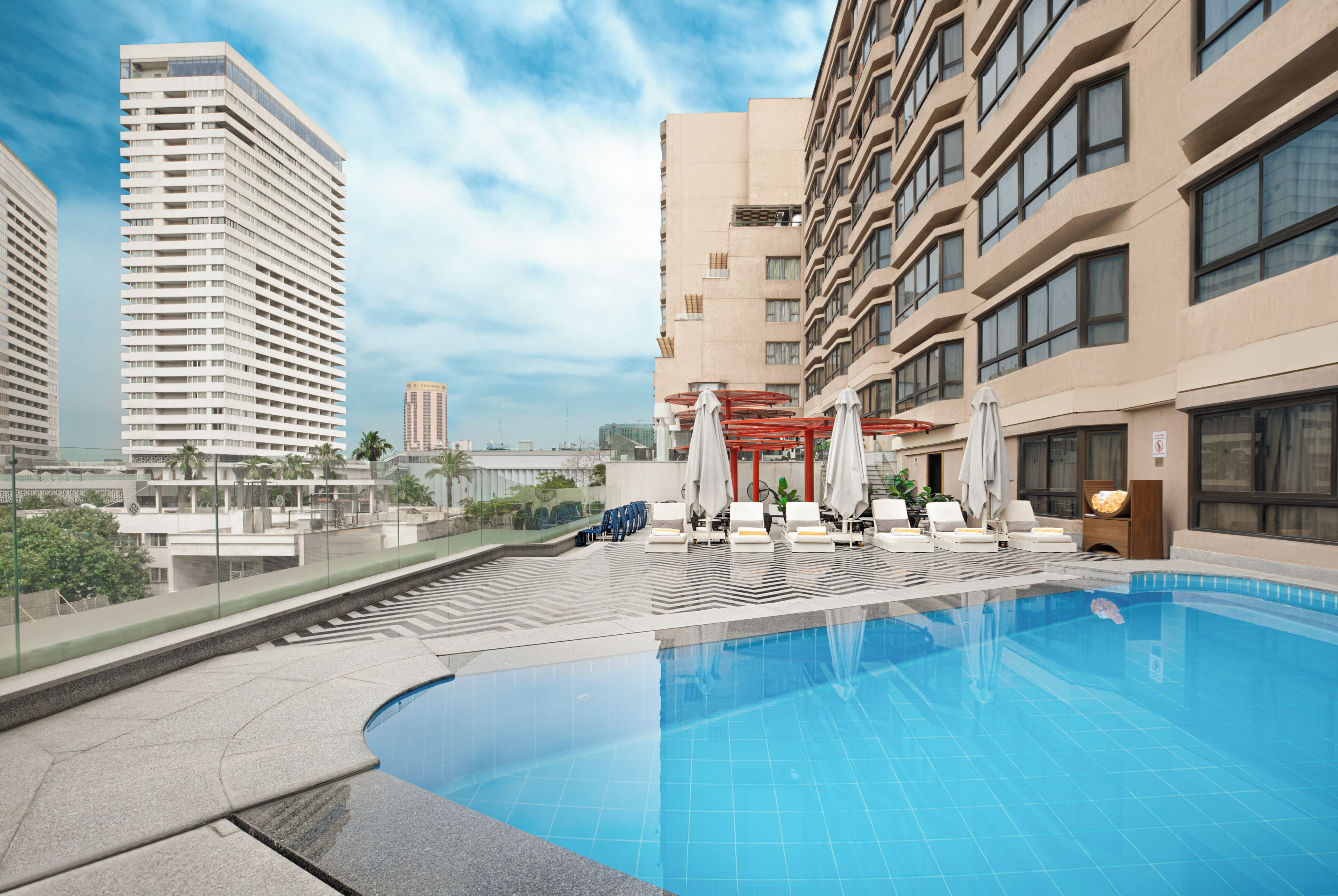 Un hôtel moderne doté d’une piscine sur le toit, de chaises longues et offrant une vue sur les bâtiments environnants.