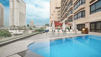 A modern hotel with a rooftop pool, lounge chairs, and a view of surrounding buildings.