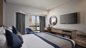 A modern hotel room with a large bed, a desk, a chair, and a TV.