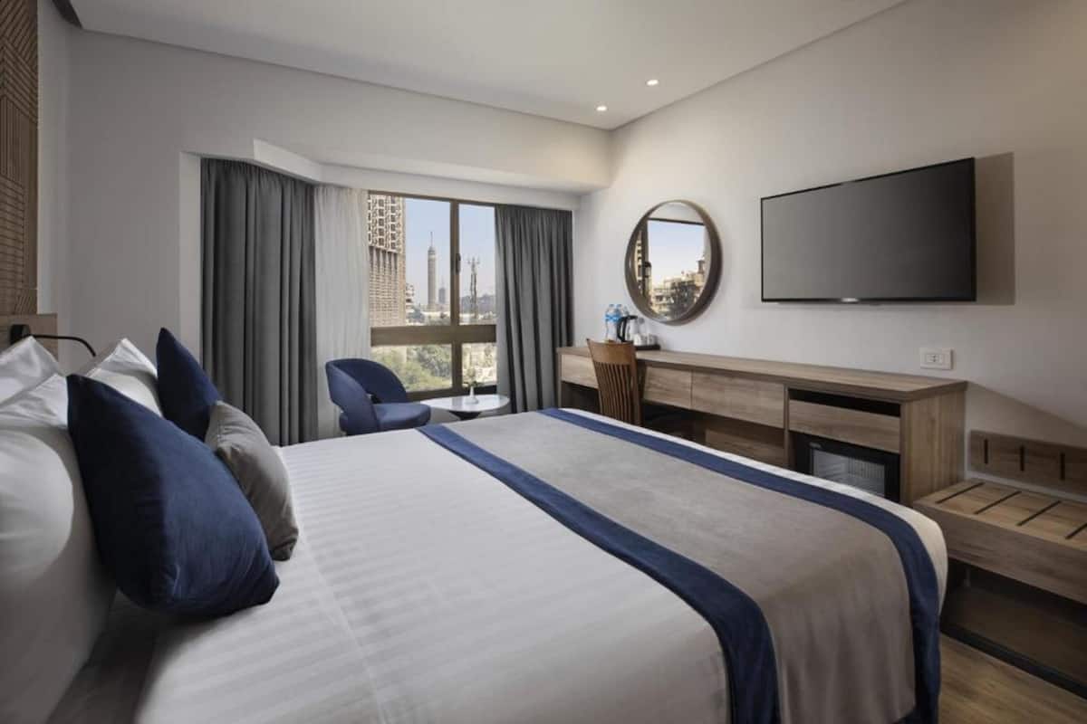 A modern hotel room with a large bed, a desk, a chair, and a TV.