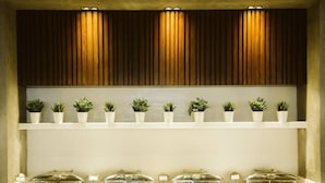 A buffet setup with multiple food service stations and potted plants on shelves.