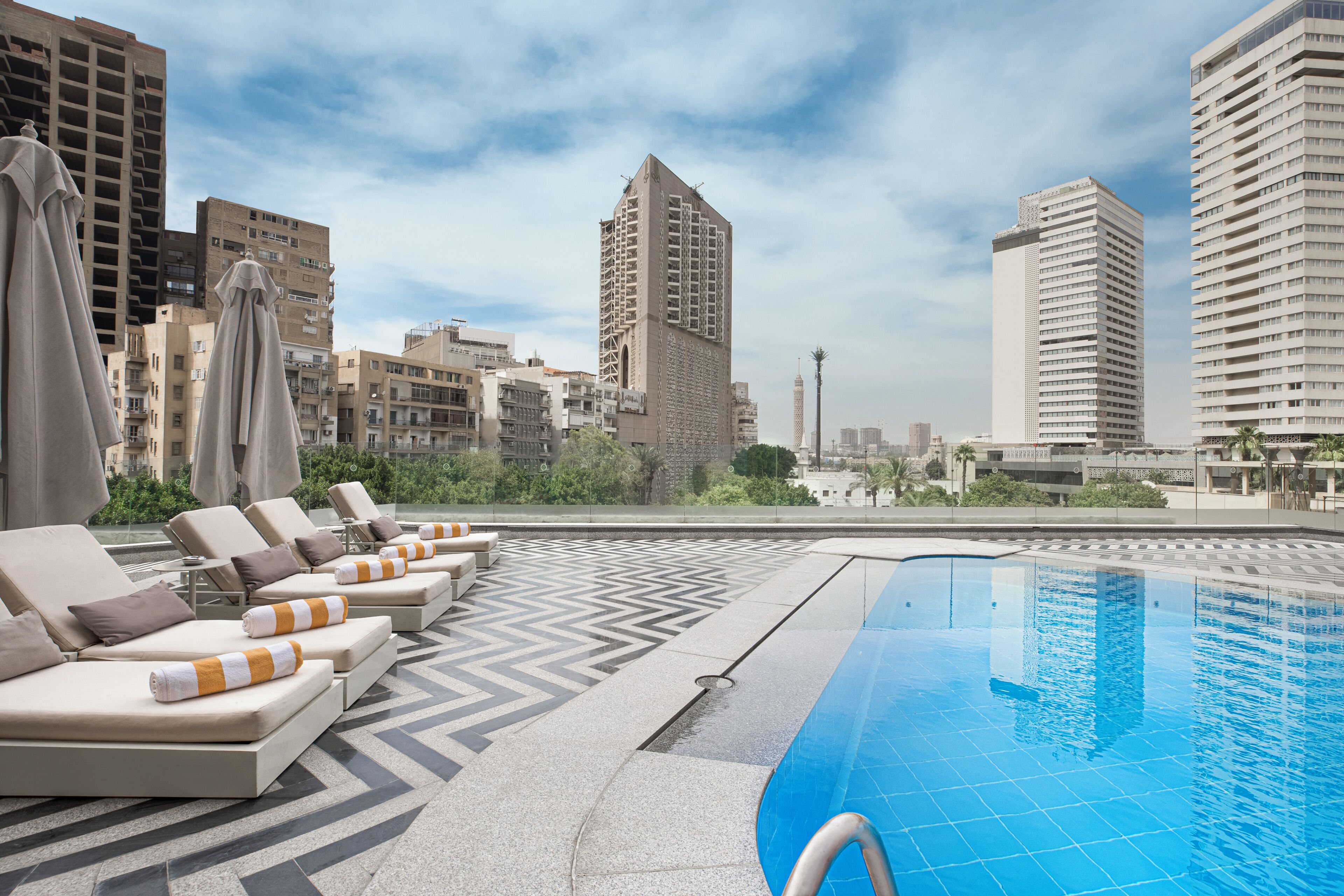 Zona de piscina en la azotea con sillones y vistas a edificios altos circundantes.