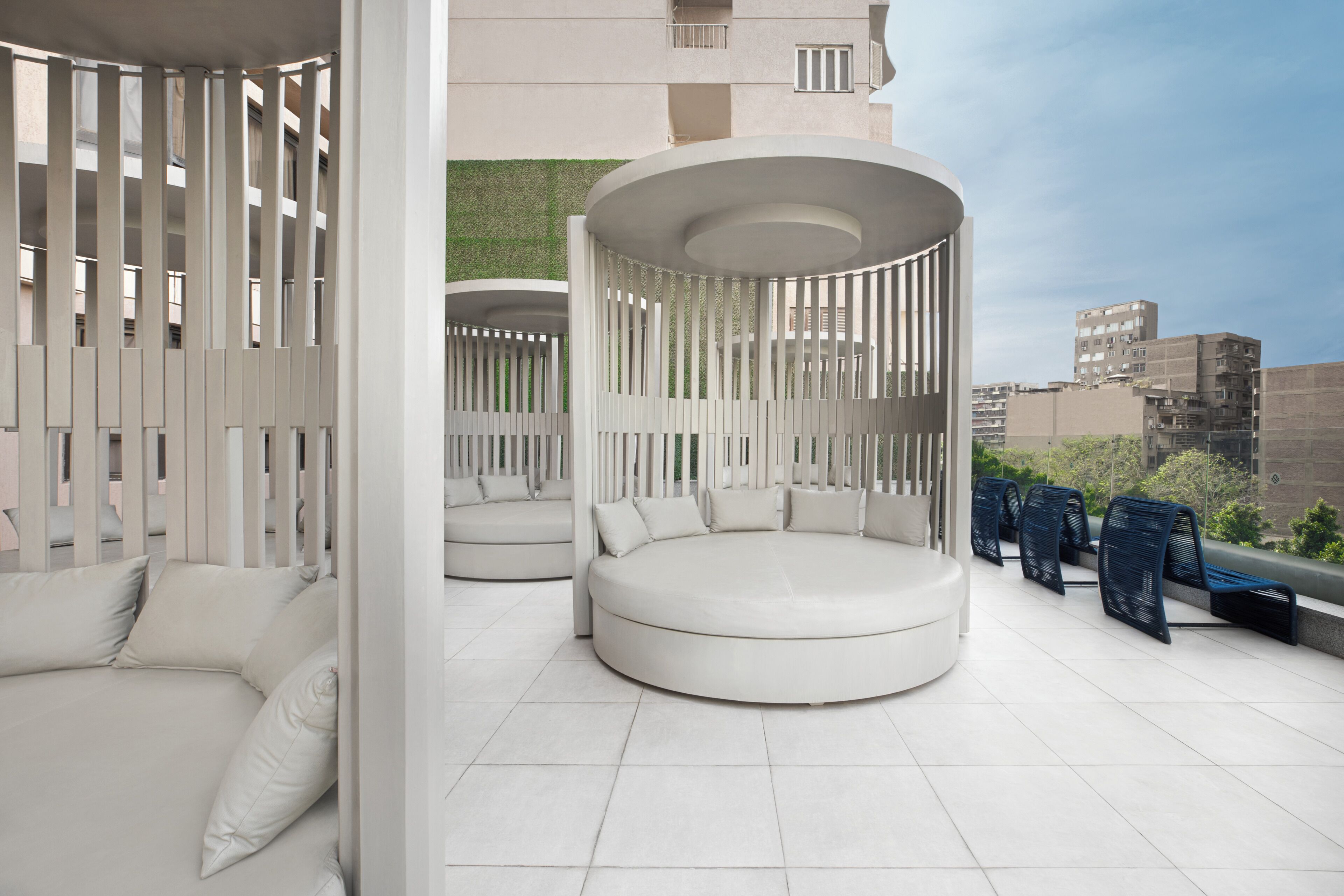 Una terraza en la azotea con zonas de estar circulares, una valla blanca y vistas a edificios.