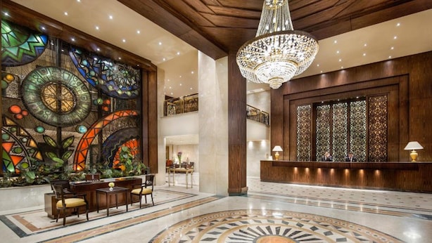 A lobby with a large stained glass wall, a chandelier, a reception desk, and a circular patterned floor.