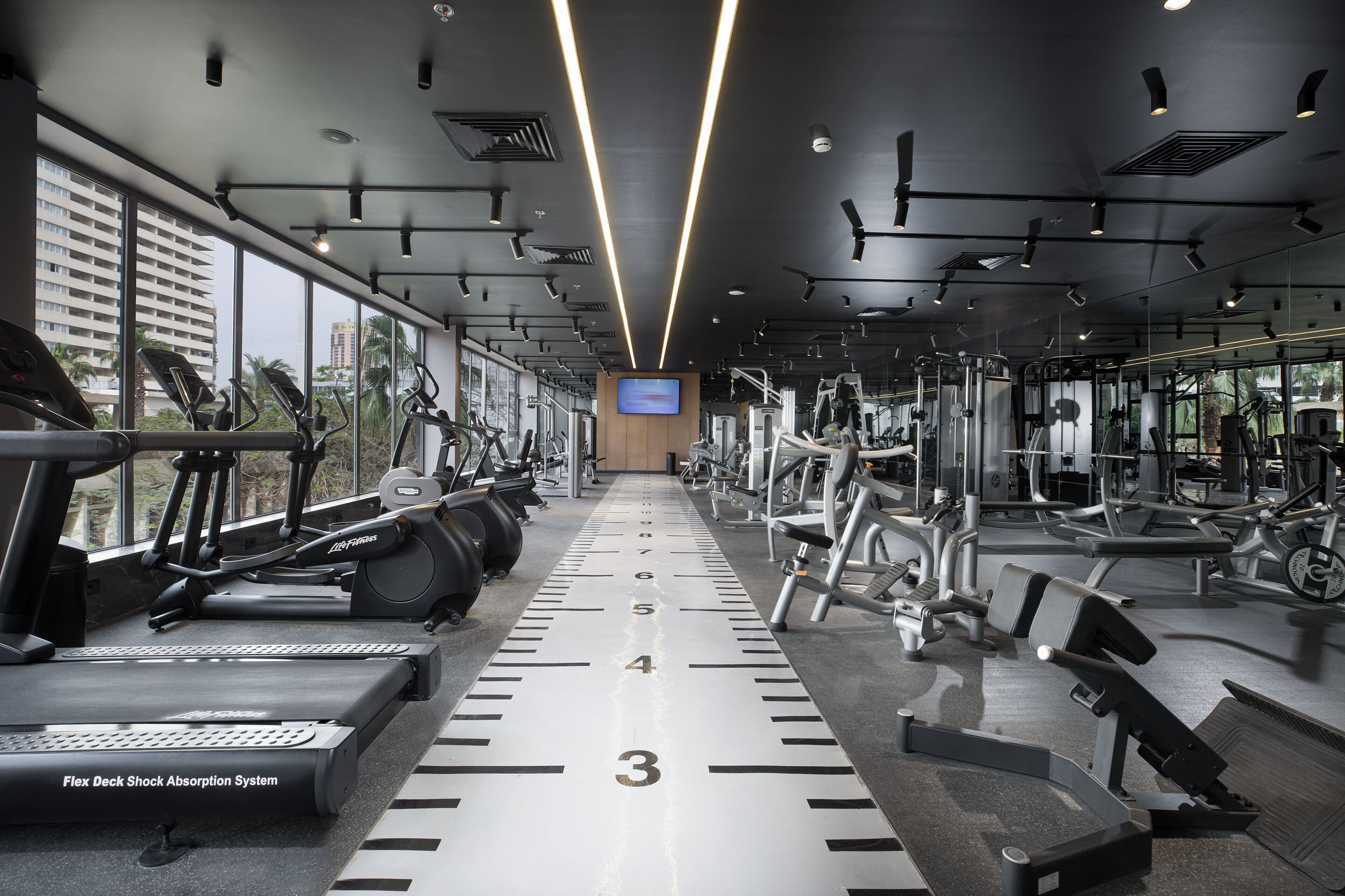 Un gimnasio con cintas de correr, máquinas de pesas y un amplio ventanal con espejos.
