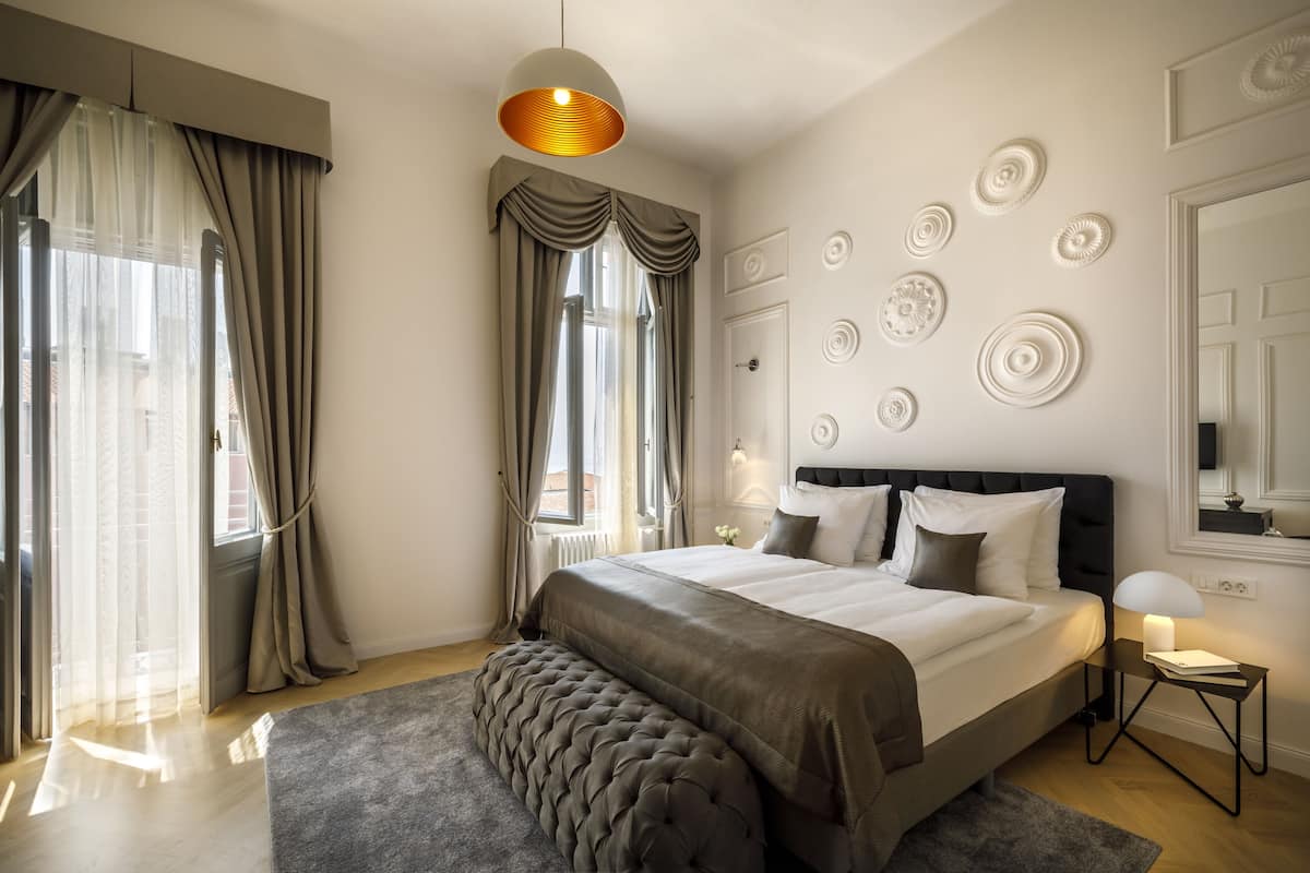 Une chambre moderne avec un grand lit, une table de chevet avec une lampe et une vue sur la ville par la fenêtre.