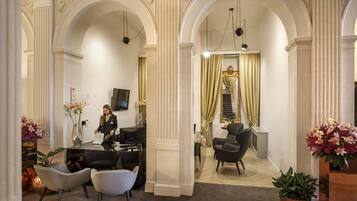 Een hotellobby met een receptiebalie, een zithoek en decoratieve zuilen.
