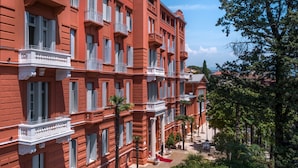 Un hôtel à plusieurs étages, avec des façades en briques rouges, des balcons blancs et un tapis rouge à l’entrée.