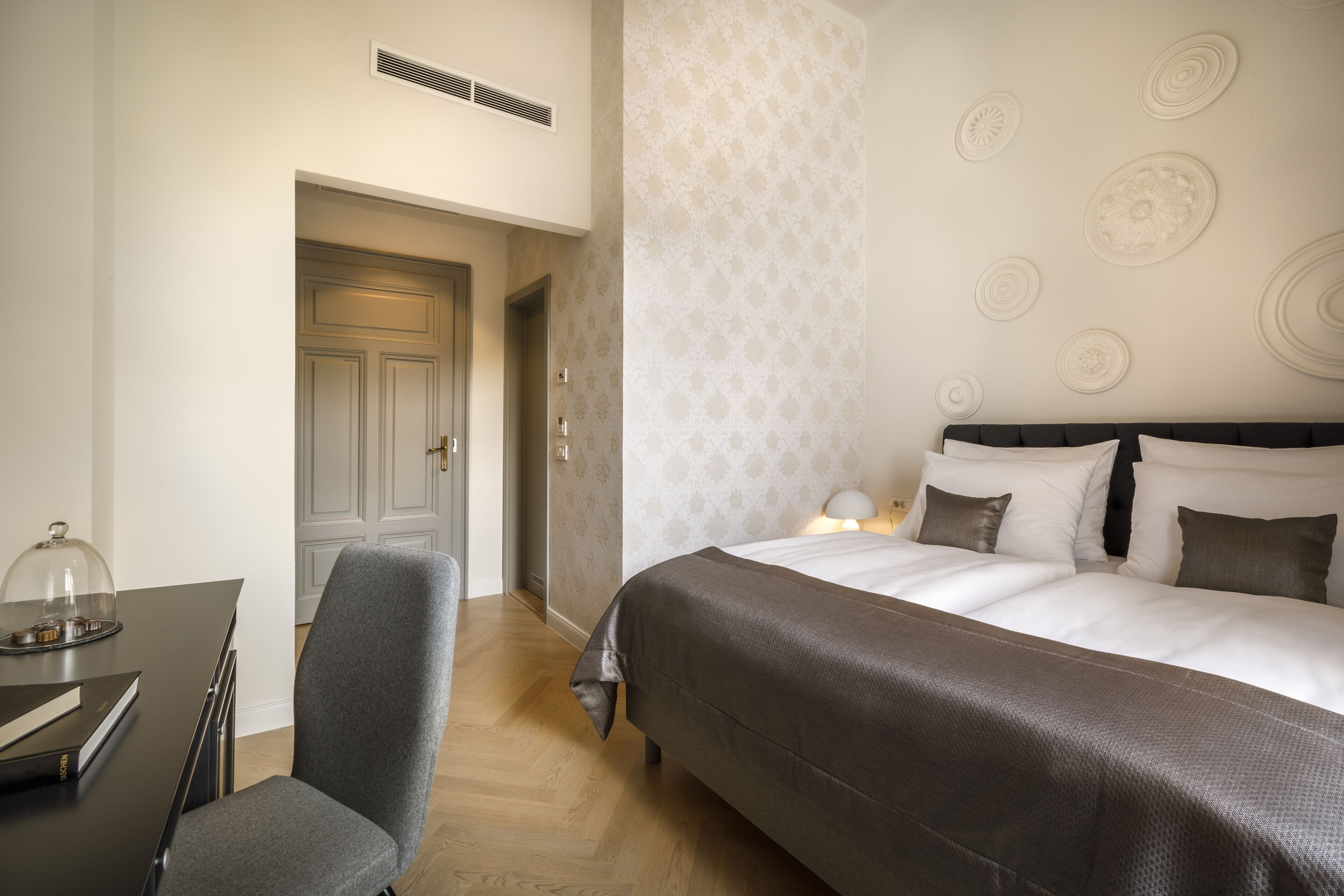 A hotel room with a bed, a desk with a chair, and a door leading to another room.