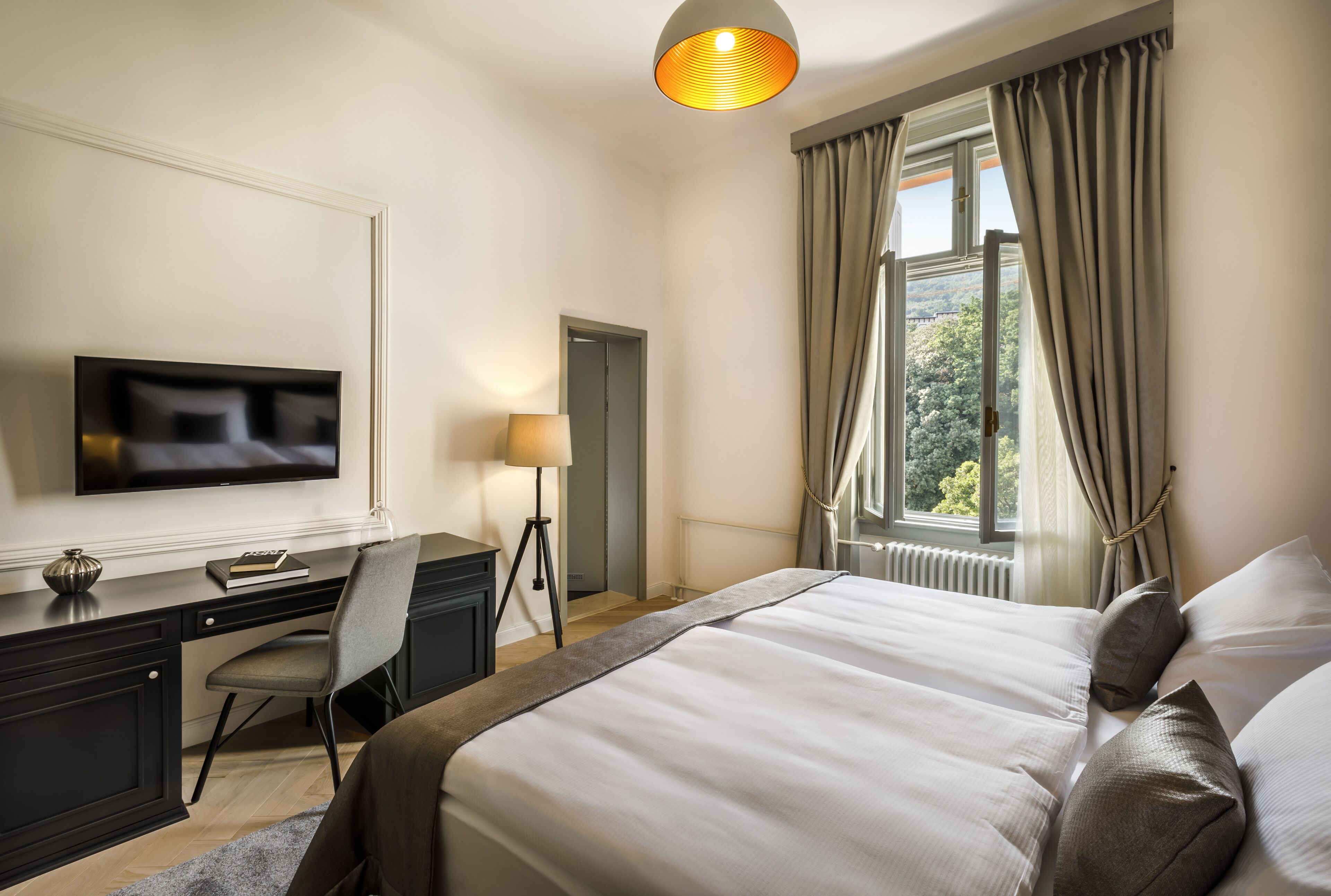Habitación de hotel con cama, escritorio con silla, televisor y ventana con cortinas.