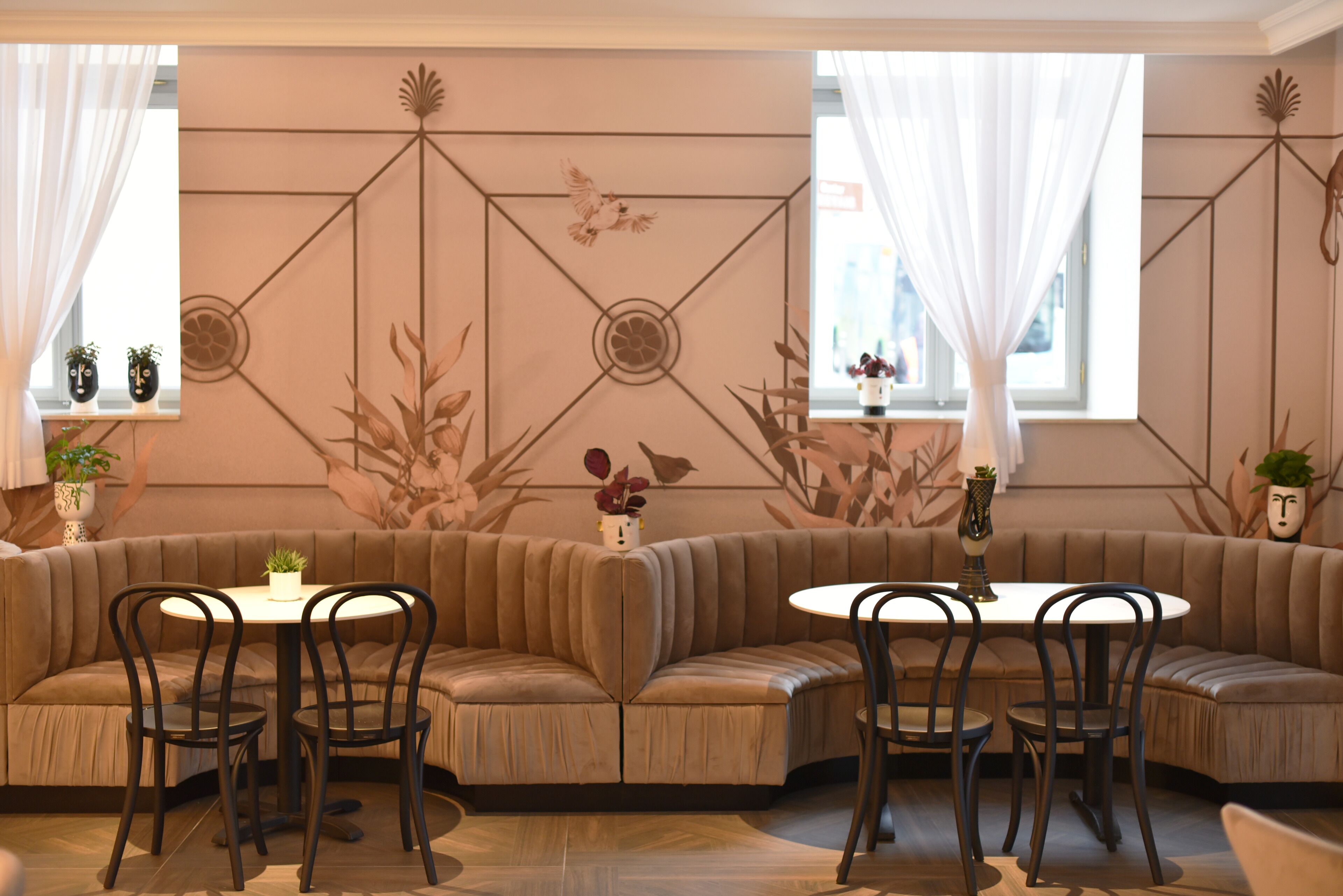A modern interior with a curved sofa, round tables, and chairs. There are decorative wall panels and potted plants.