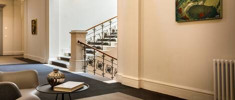 A modern interior with a staircase, a painting, and a table with a book and vase.