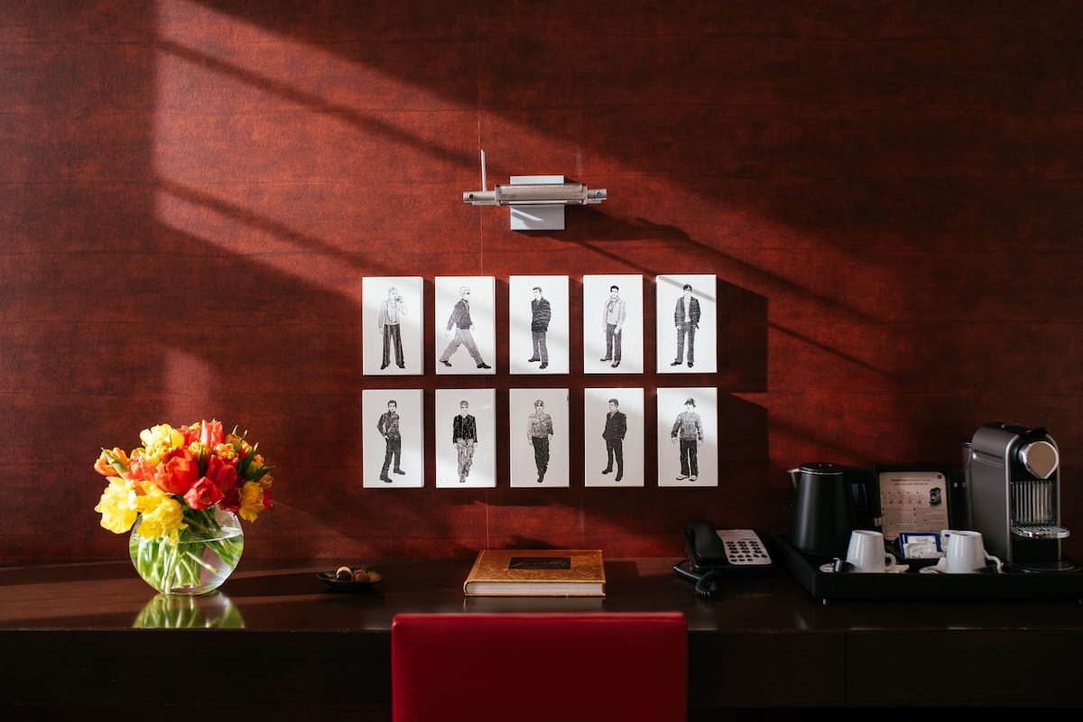 A desk with a vase of flowers, a book, a coffee maker, and a wall with framed pictures.