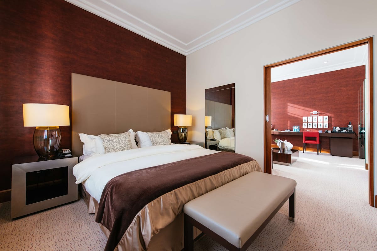 A hotel room with a large bed, bedside lamps, a desk with a chair, and a mirror.