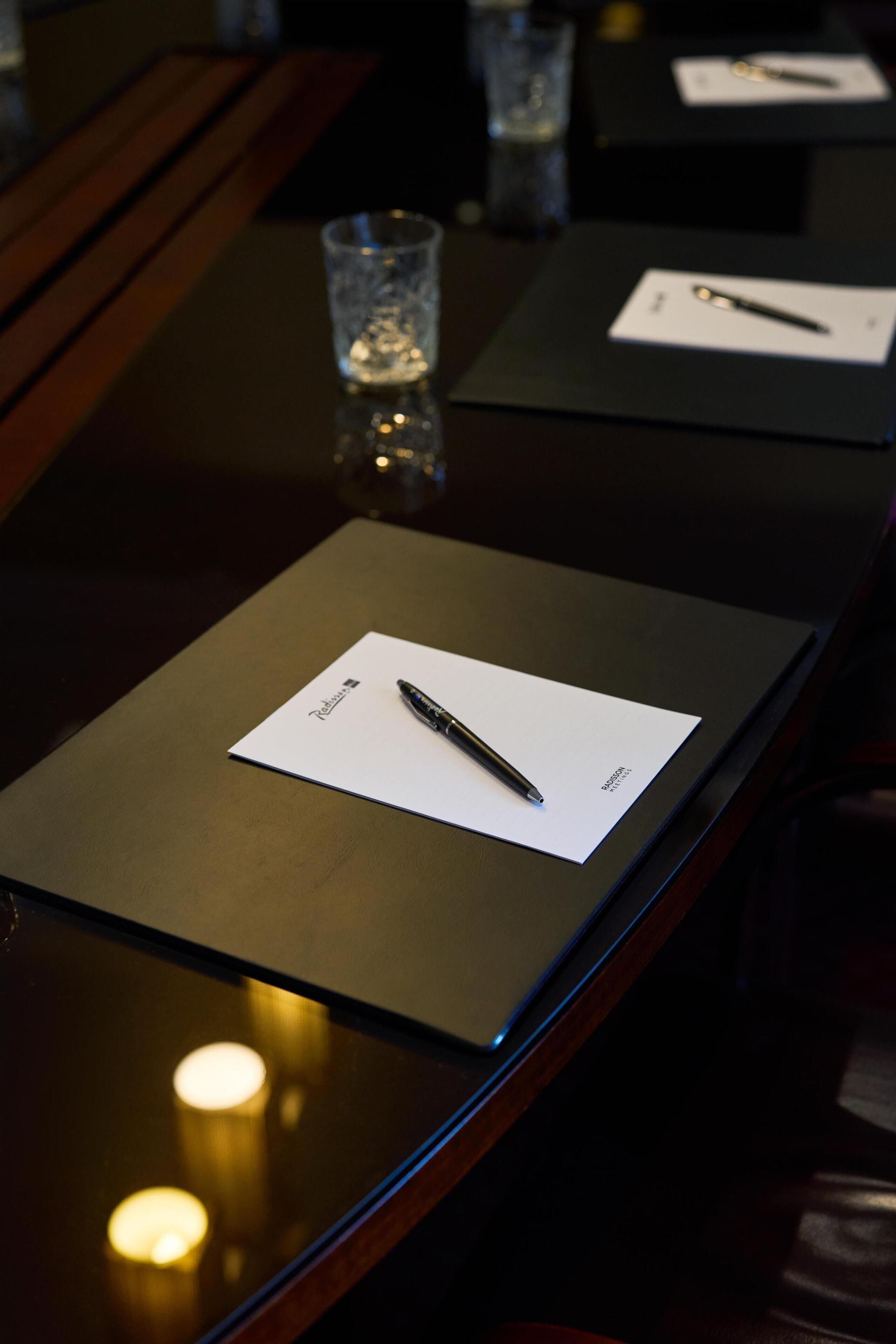 A table with a pen on a piece of paper, a glass of water, and a candle.