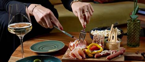 A dining table with a glass of white wine, a bowl of olives, a plate of sliced meats, and a small vase with flowers.
