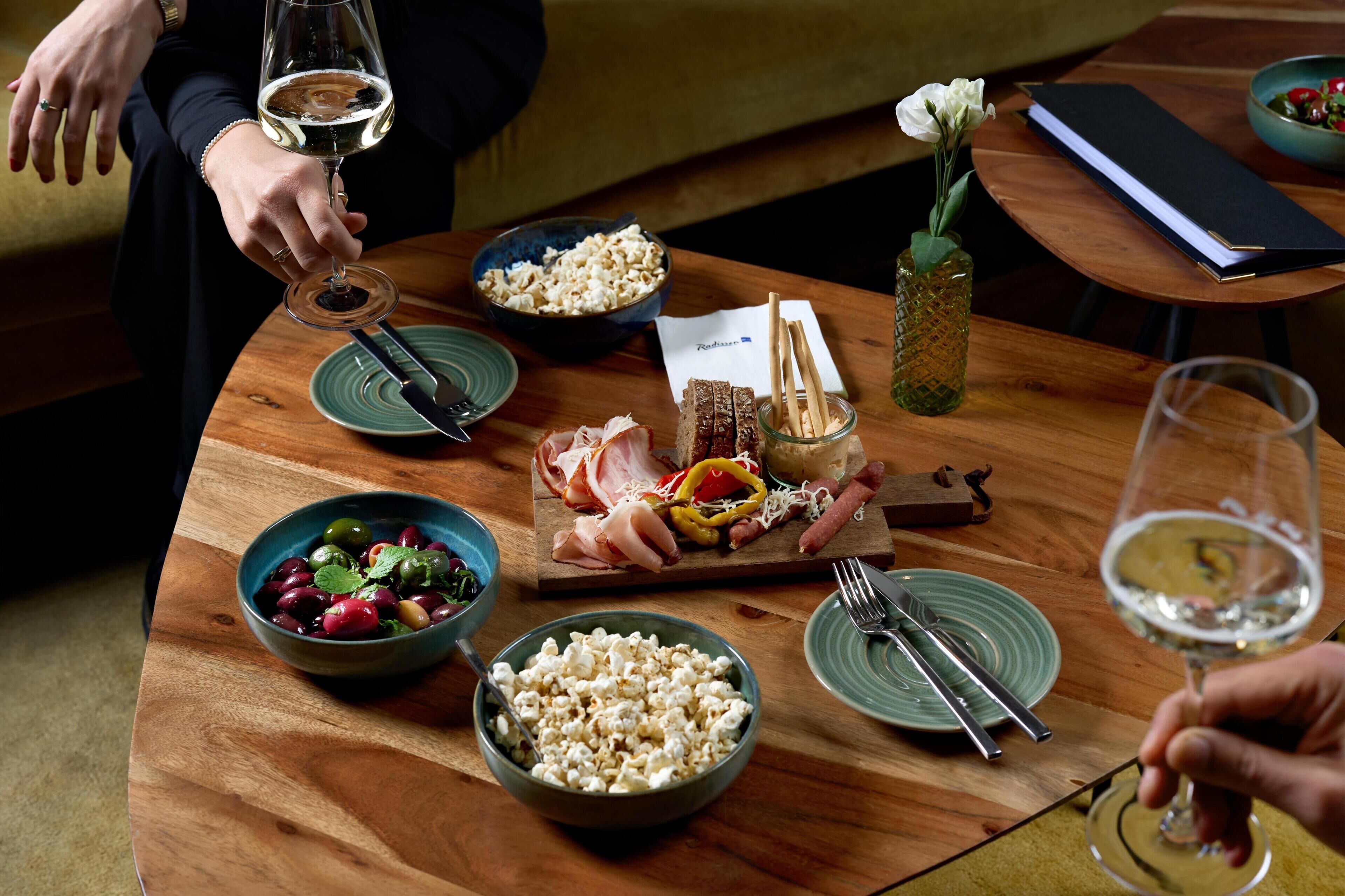 Uma mesa de madeira com diversos alimentos, um copo de vinho branco e um cardápio.