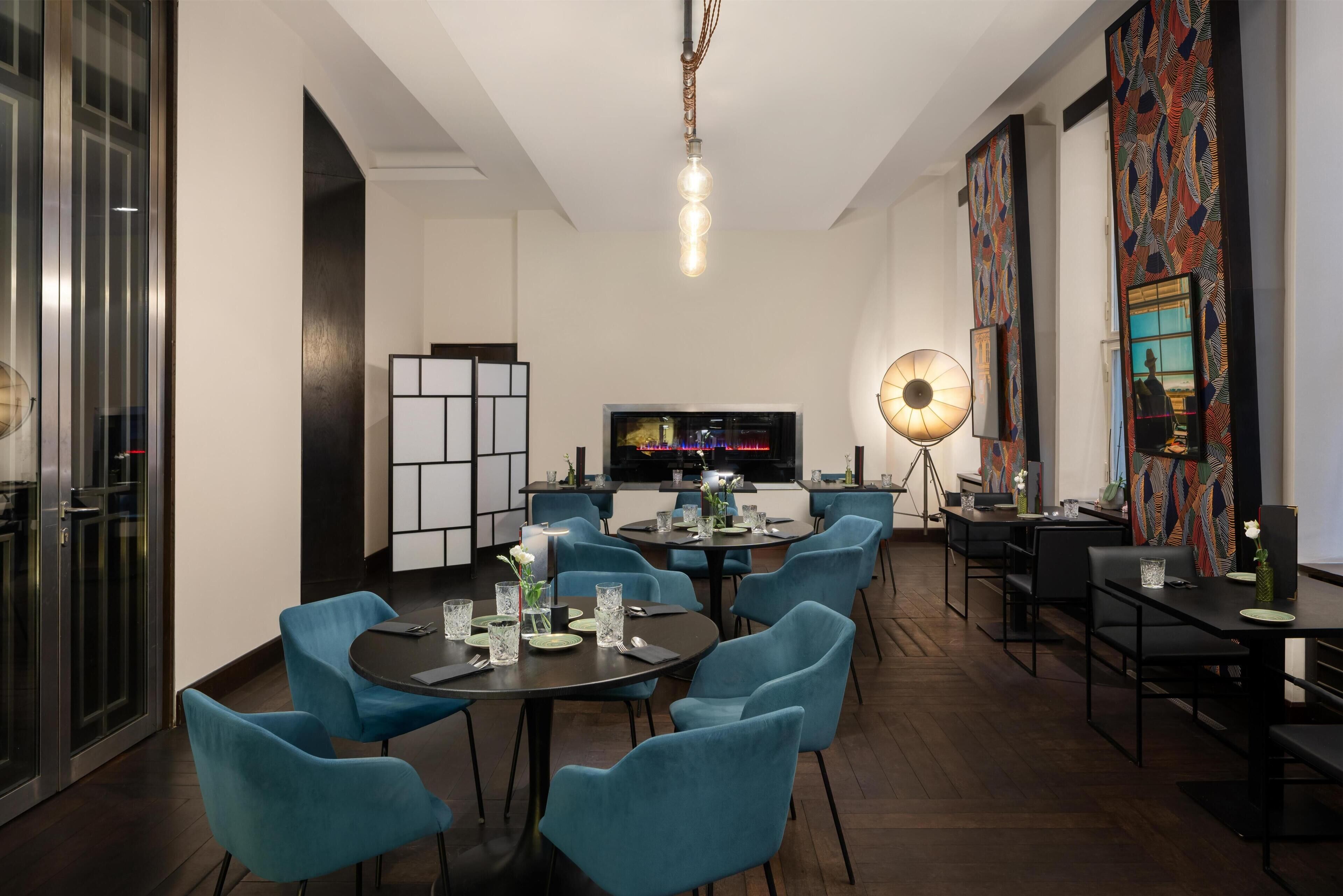 A modern dining area with round tables, blue chairs, and a large screen.