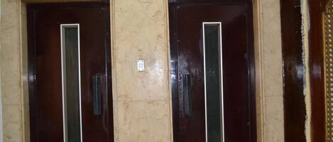 Two dark wooden doors with vertical glass panels, set in a beige marble wall.