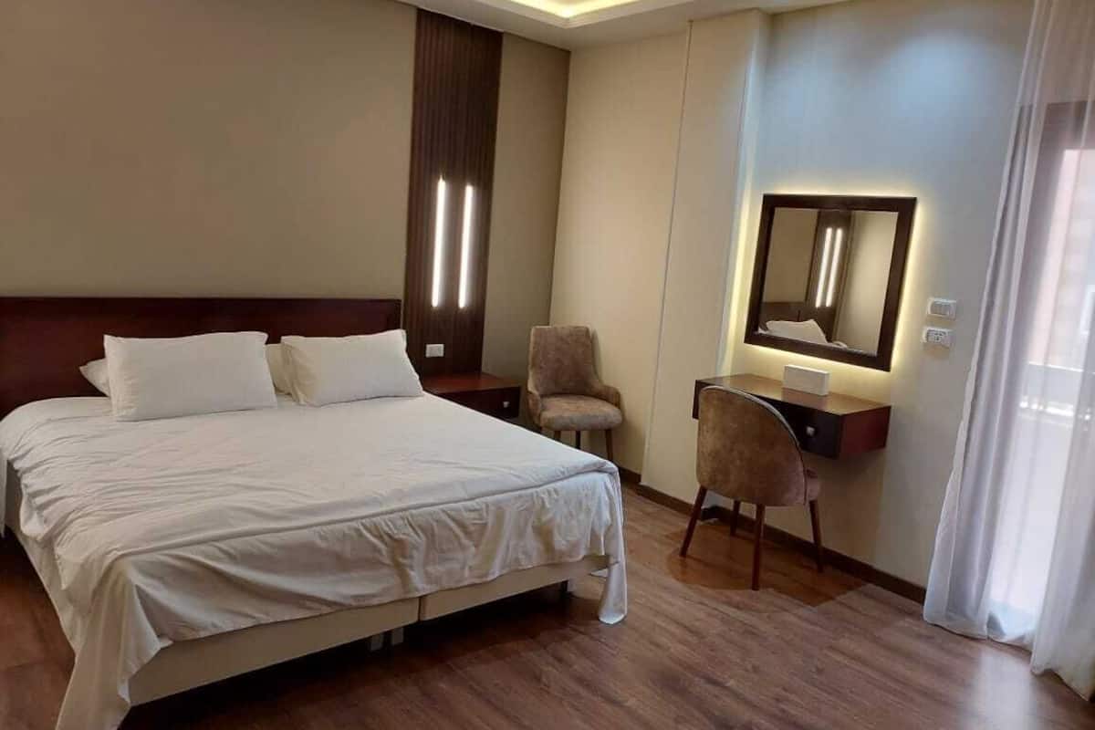 A hotel room with a large bed, a desk with a chair, a mirror, and a nightstand.
