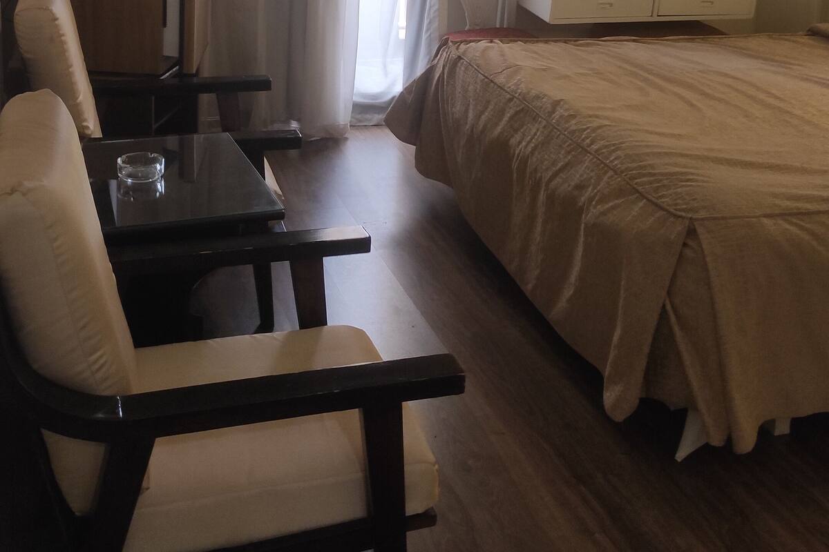 A hotel room with a bed, a desk, a chair, a mirror, and a window with curtains.