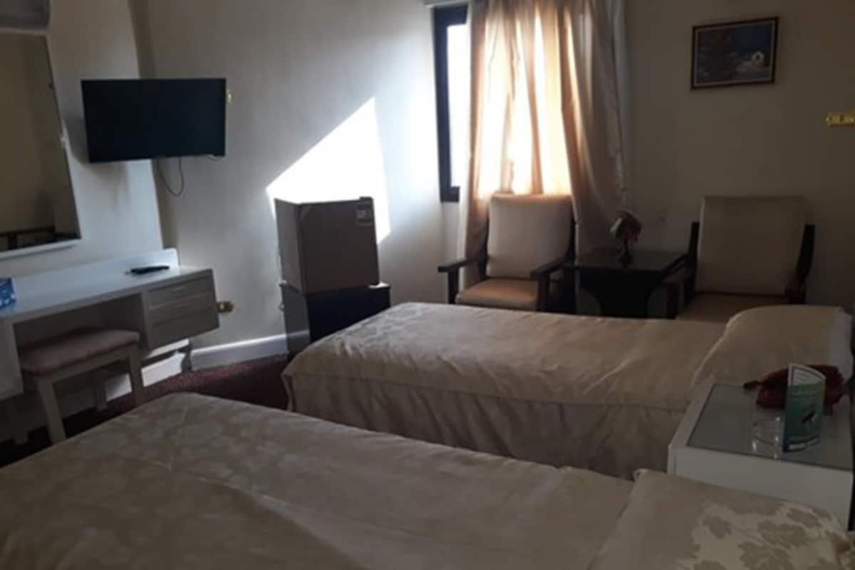 A hotel room with two beds, a desk with a chair, a television, and a window with curtains.