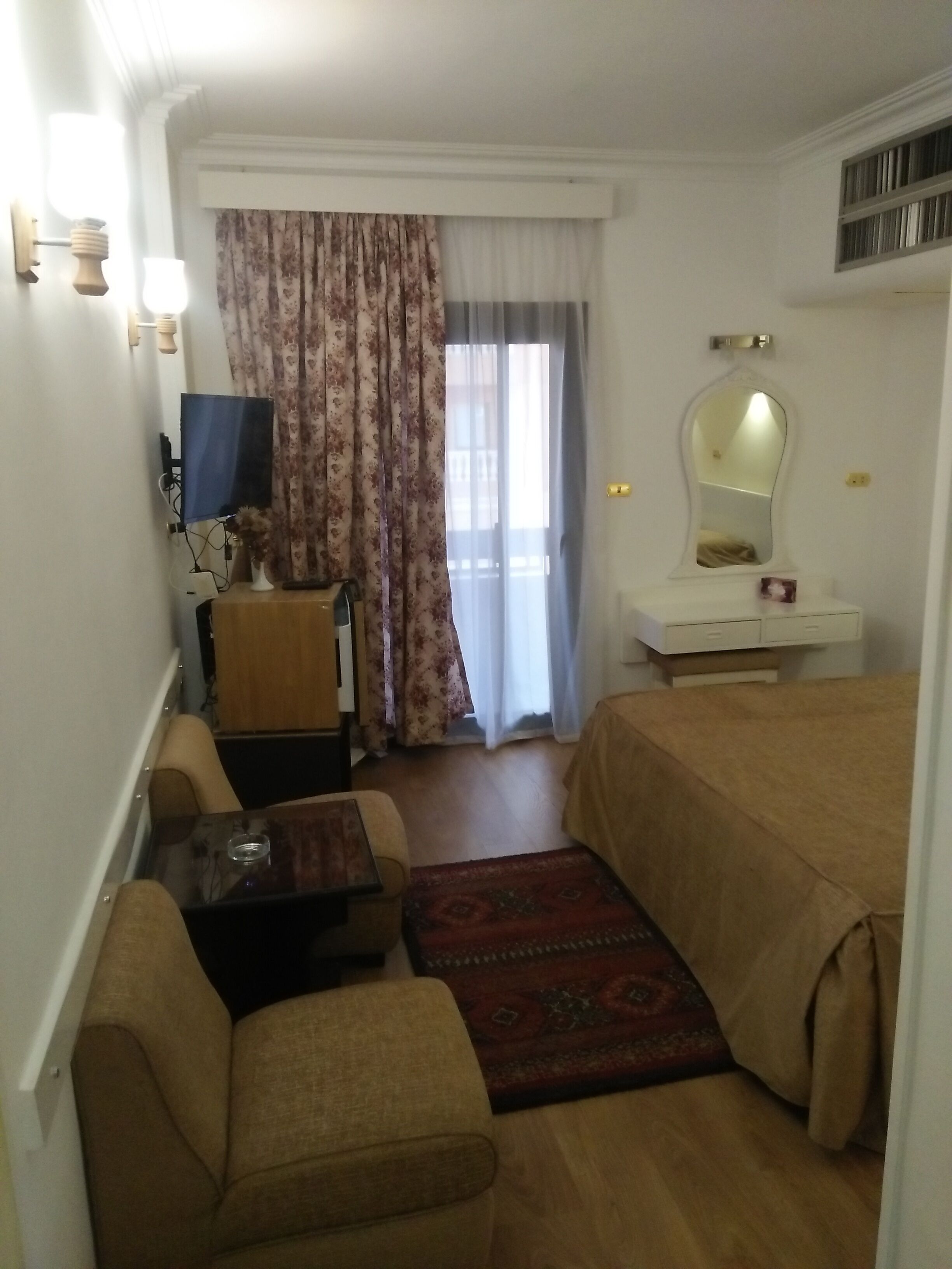 A hotel room with a bed, a desk, a chair, a television, and a window with curtains.