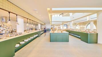 Un vaste espace de restauration proposant de nombreux comptoirs de service et une île centrale, avec un design moderne agrémenté de touches de vert et d’un éclairage abondant.