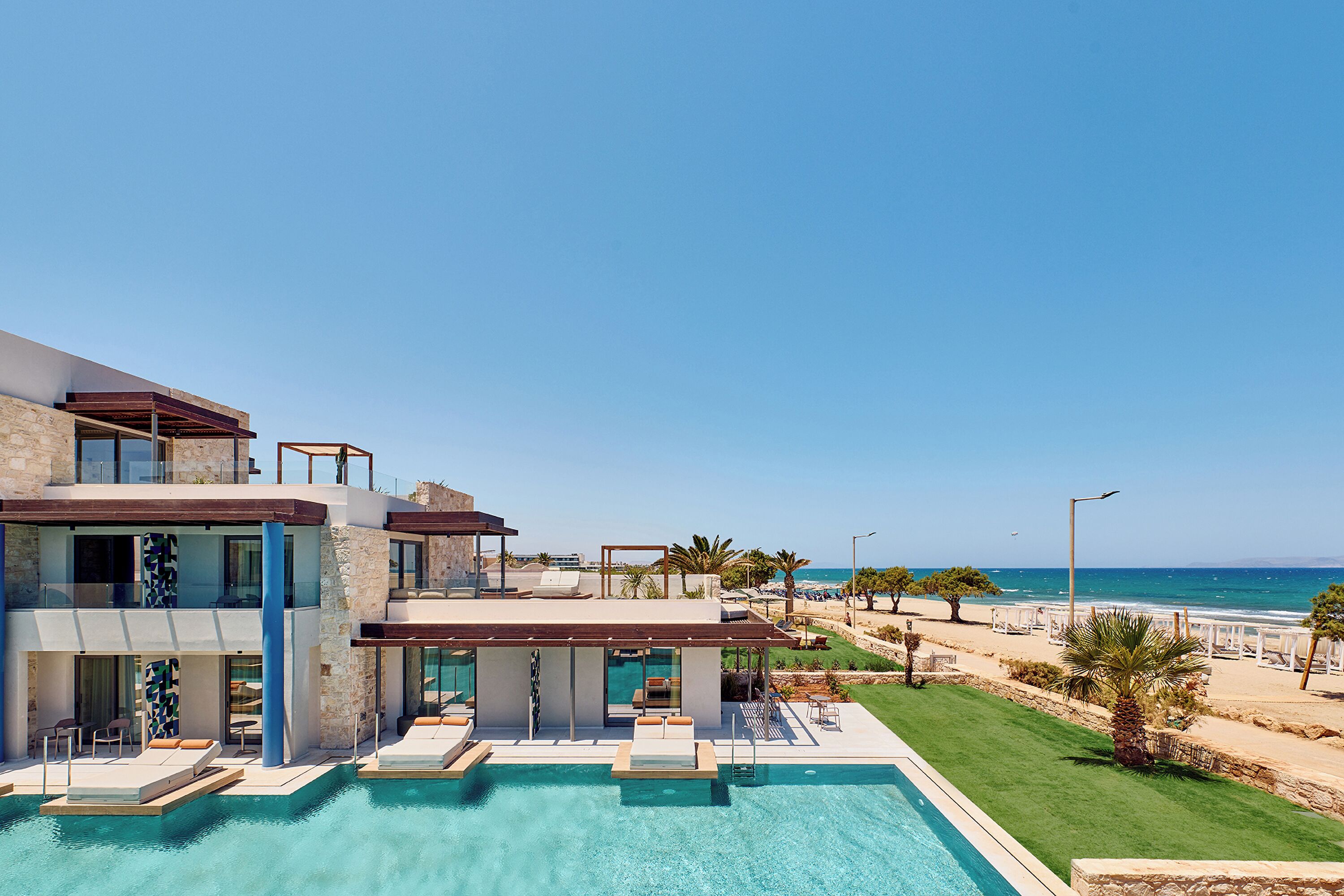 A modern hotel with a pool, a beach view, and a well-maintained lawn.