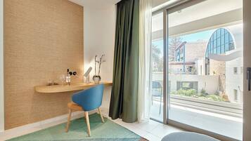 Quarto moderno com escrivaninha de madeira, cadeira azul, janela grande com vista para edifícios e cortina verde.