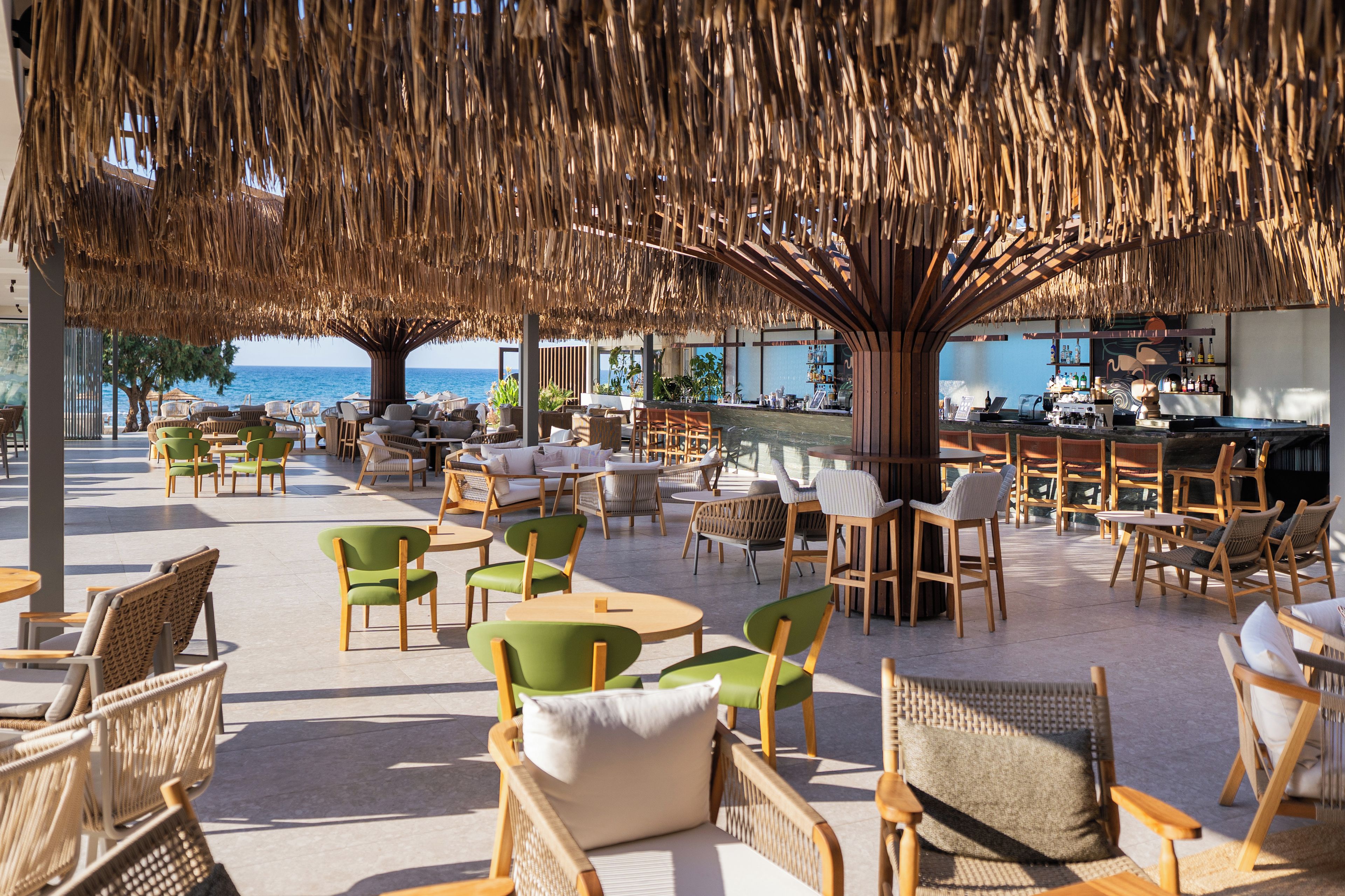 Un área de estar al aire libre con sillas y mesas de mimbre, un bar y vistas al mar.